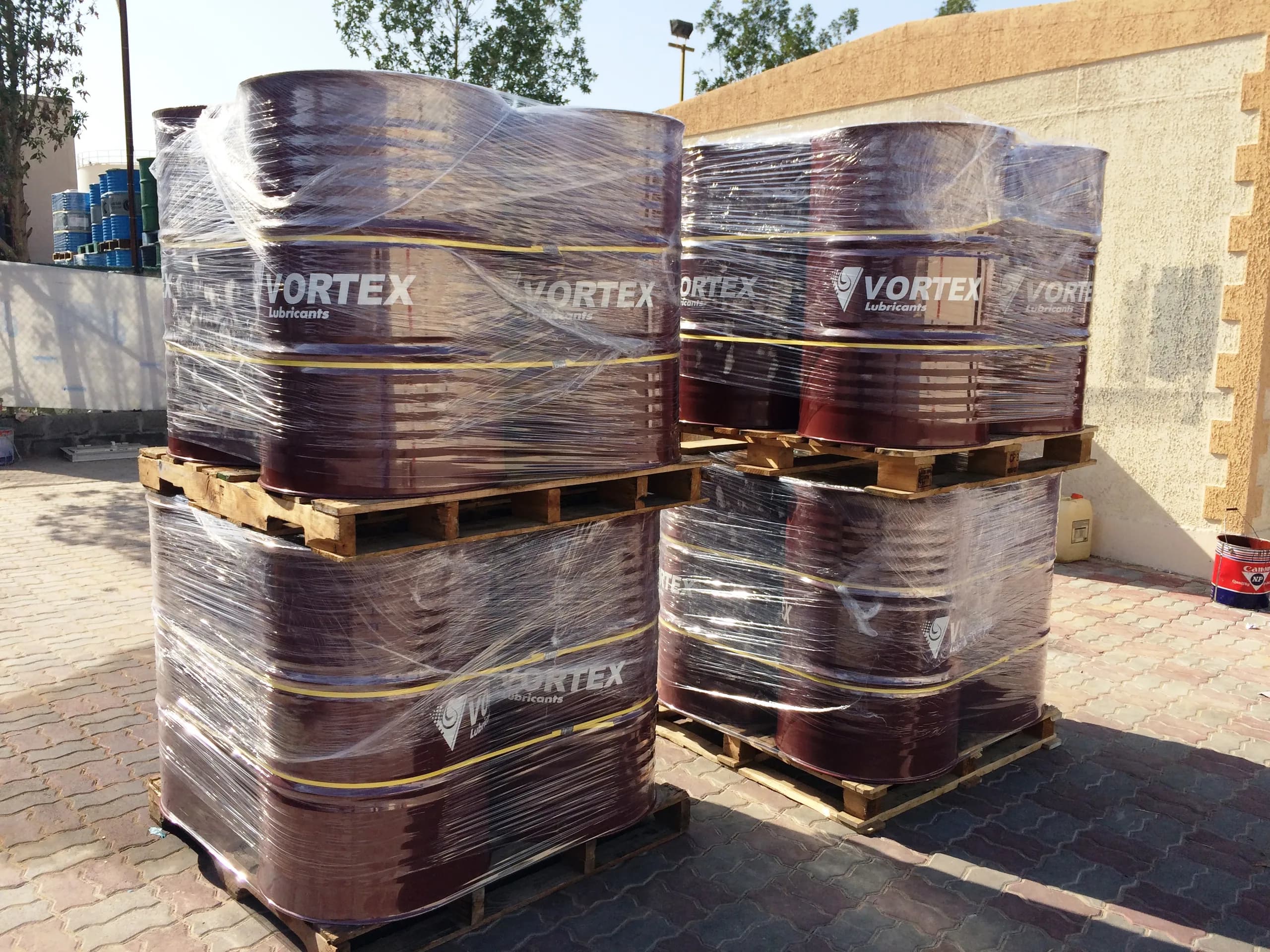 Shrink-wrapped pallets of oxblood Vortex drums strapped in yellow, stacked in the yard