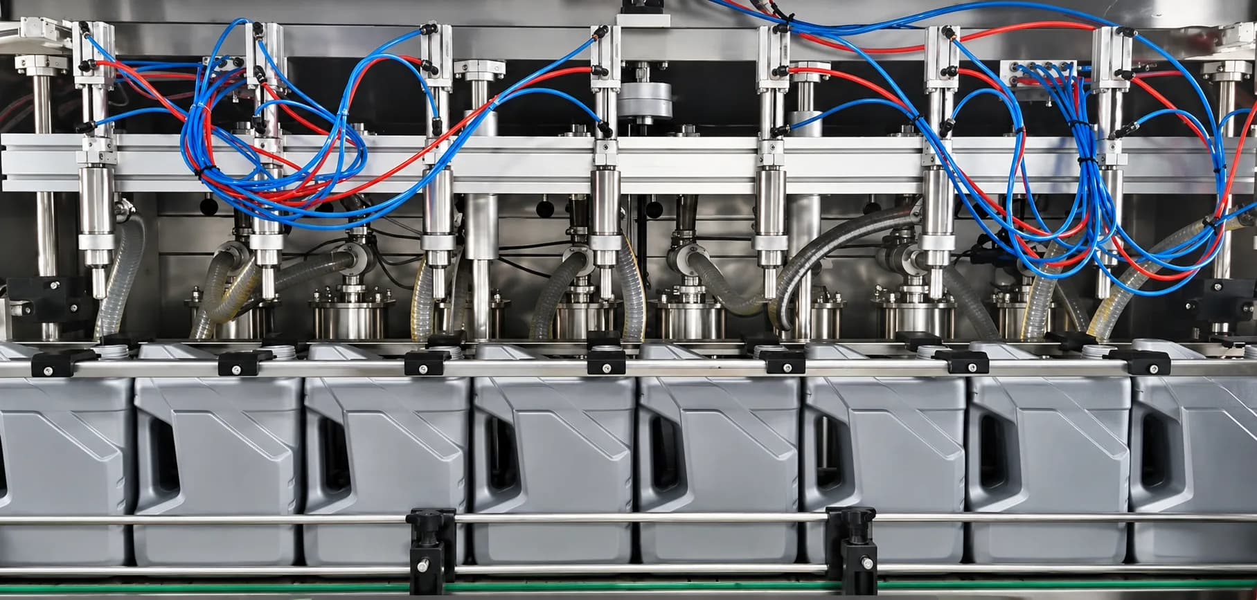 Filling heads lowered over a row of jerrycans on the line, with blue and red pneumatic lines above