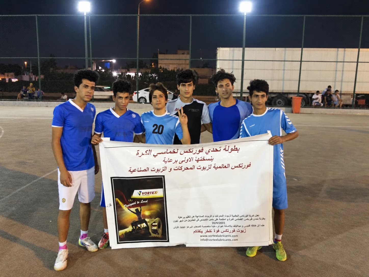 Six players in blue holding the tournament banner at the side of the pitch