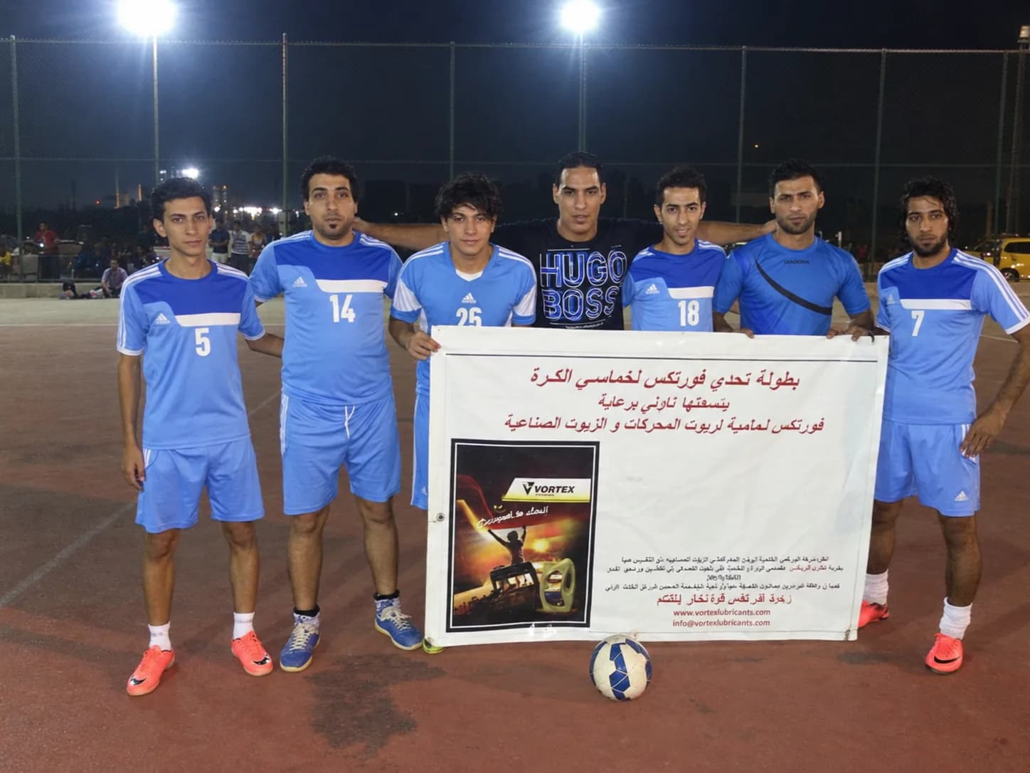 Seven players in pale blue with the tournament banner and a match ball at their feet